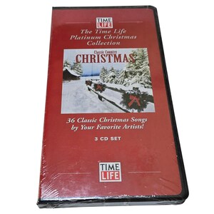 Puede incluir: Un set de CD Time Life Platinum Christmas Collection. La caja roja presenta el texto "Classic Country Christmas" y una escena invernal. El set incluye 36 canciones clásicas de Navidad.