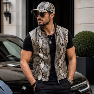 Op de afbeelding: Een vest en baseballpet met slangenpatroon. Het vest heeft een ritssluiting en wordt over een zwart t-shirt gedragen. De pet heeft een gebogen klep. De persoon draagt een zonnebril en een zilveren ketting. De outfit wordt gecombineerd met een zwarte broek.