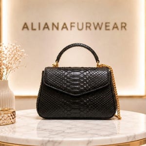 Puede incluir: Bolso de mano negro con estampado de piel de serpiente, asa superior y correa de cadena dorada. El bolso tiene cierre de solapa y herrajes dorados. El nombre de la marca "ALIANAFURWEAR" se muestra en el fondo.