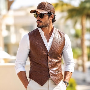 May include: A brown leather vest with a textured pattern, worn over a white shirt. The vest has a button-up front and a V-neck design. A matching brown leather baseball cap and sunglasses complete the look. A watch is visible on the wrist.