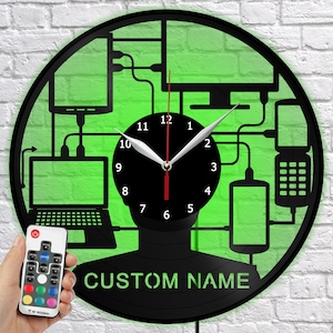 Pode incluir: Relógio de parede preto com fundo verde, apresentando a silhueta de uma pessoa com dispositivos tecnológicos conectados. O mostrador do relógio é preto com ponteiros e números brancos. O texto "CUSTOM NAME" está na parte inferior. Um controle remoto está no canto inferior esquerdo.