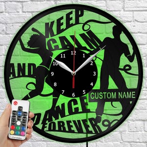 May include: Black vinyl record clock with a green background and the words "KEEP CALM AND DANCE FOREVER." Features black silhouettes of dancers and a black clock face with white hands. Includes a remote control.