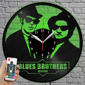 May include: Black vinyl record clock featuring a green silhouette of the Blues Brothers with the text "BLUES BROTHERS RECORDS". The clock has white hands and a red second hand. A remote control with color options is visible.