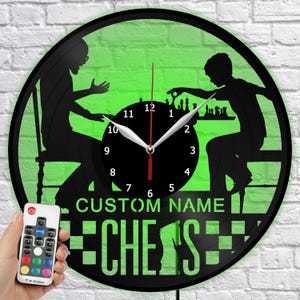 May include: Black vinyl record clock with a green background and a chess theme. The clock features silhouettes of two people playing chess, a black clock face, and the words "CUSTOM NAME" and "CHESS". A remote control is visible.