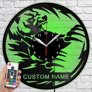 Puede incluir: Reloj de vinilo negro con un diseño de dragón verde. El reloj tiene manecillas blancas y un segundero rojo. El texto "CUSTOM NAME" se muestra en la parte inferior. Un mando a distancia está en la imagen.