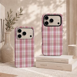 May include: Two smartphone cases featuring a pink, white, and beige plaid pattern. Each case has a black camera cutout frame with three circular lens openings. The cases are designed with a flat, rectangular shape and a consistent grid design.