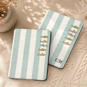 Peut inclure: Deux étuis rectangulaires pour liseuse avec un motif à rayures verticales bleu clair et blanc. Chaque étui est orné d'une colonne de petites illustrations de poissons colorés. Un étui affiche les initiales EM en noir en bas.
