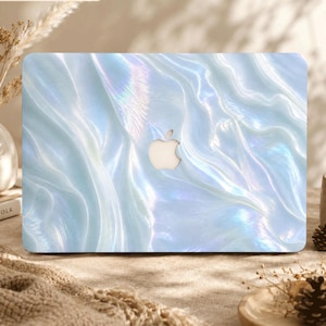 May include: A laptop cover featuring a light blue and white iridescent, pearlescent finish with a wavy, fluid pattern. The surface has a glossy, reflective quality that mimics the appearance of mother-of-pearl, with a central cutout for an Apple logo.