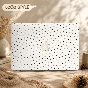 Peut inclure: Une coque rigide pour ordinateur portable de couleur blanche avec un motif de petits points noirs répartis sur toute la surface. La coque présente une découpe centrale révélant le logo Apple argenté. Le texte "LOGO STYLE" est imprimé en haut à gauche.