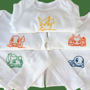 May include: A collection of five white long-sleeved baby bodysuits, each featuring a different embroidered character design. The designs include a yellow Pikachu, an orange Charmander, an orange Charizard, a green Bulbasaur, and a blue Squirtle.