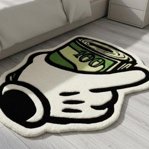 May include: A tufted rug shaped like a cartoon hand pointing a finger while holding a rolled-up green one hundred dollar bill. The design features bold black outlines, a white hand, and green currency details with the number 100 clearly visible.