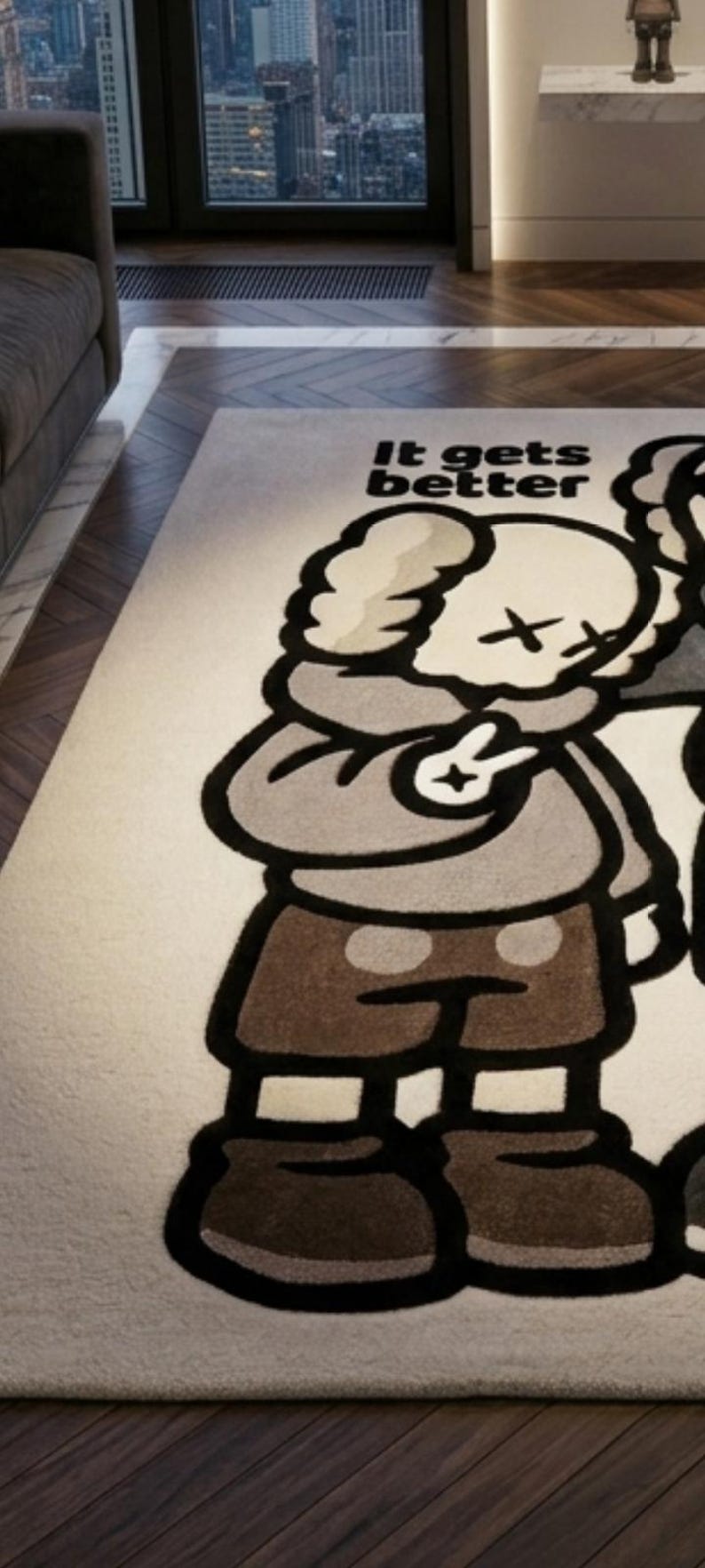 May include: A rectangular area rug featuring a cream-colored background with a large, stylized cartoon character graphic in shades of brown, gray, and black. The character has X-shaped eyes and is making a peace sign. The text "It gets better" is printed.