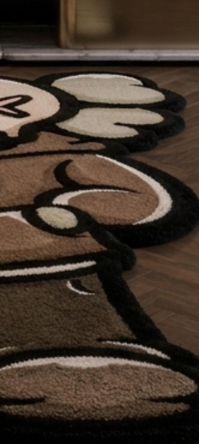 May include: A tufted rug featuring a stylized cartoon character design with thick black outlines. The rug is composed of brown, beige, and cream-colored yarn sections, creating a textured, multi-layered appearance with rounded, organic shapes.