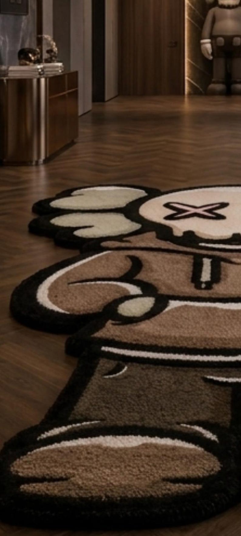 May include: A tufted area rug shaped like a cartoon character with a brown hoodie, tan face, and black outlines. The character features X-shaped eyes, white gloved hands, and a brown lower body section, all rendered in a plush, textured pile material.