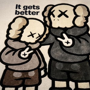 May include: A tufted rug featuring two cartoon characters with X-shaped eyes, one comforting the other. The characters wear hoodies and shorts in shades of gray and brown. The text "It gets better" is printed in black in the upper left corner.