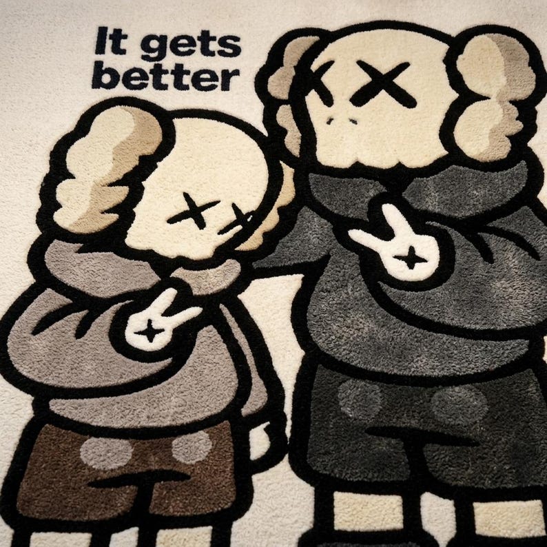 May include: A tufted rug featuring two cartoon characters with X-shaped eyes, one comforting the other. The characters wear hoodies and shorts in shades of gray and brown. The text "It gets better" is printed in black in the upper left corner.