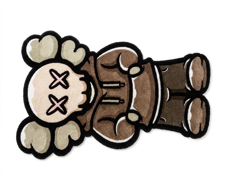 May include: A tufted rug shaped like a cartoon character with a skull-like head, cross-shaped eyes, and cloud-like ears. The figure wears a brown hooded sweatshirt and dark brown pants, outlined in thick black yarn with a soft, textured surface.