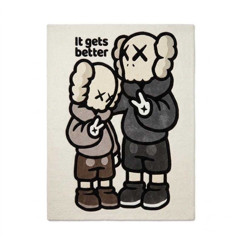 May include: A rectangular off-white throw blanket featuring a graphic illustration of two cartoon figures with X-shaped eyes. The larger figure wears a dark gray hoodie and shorts, while the smaller wears a light gray hoodie. Text reads: It gets better.