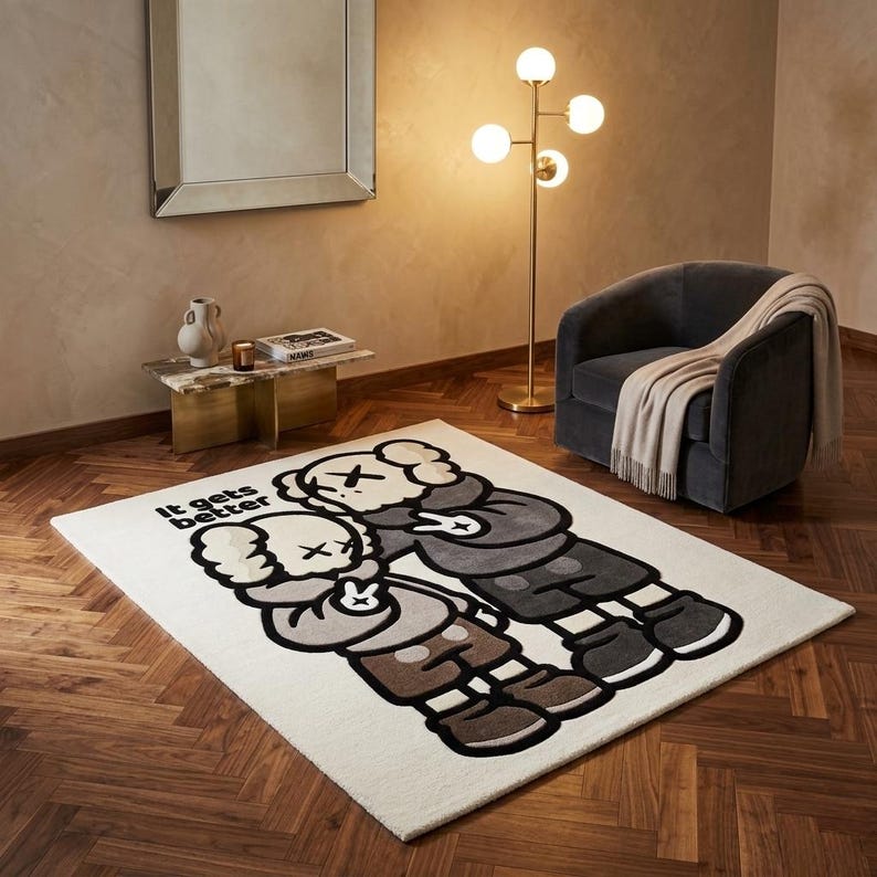 May include: A rectangular area rug featuring a cream background with a large graphic illustration of two cartoon characters in shades of gray and brown. The characters are making peace signs, and the text "It gets better" is printed in black.
