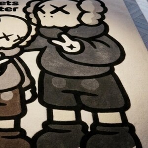May include: A rectangular area rug featuring a large graphic illustration of two cartoon characters with X-shaped eyes. The characters are rendered in shades of gray, brown, and black on a light beige background. The text ets ter is visible.