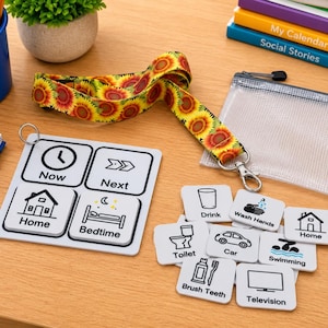 May include: A visual schedule board with four squares labeled Now, Next, Home, and Bedtime, accompanied by a sunflower lanyard and several square tiles featuring icons and text for daily activities like Drink, Wash Hands, Toilet, Car, Swimming, and Brush Teeth.