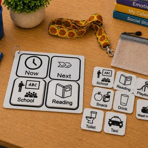 Könnte beinhalten: Ein weißes, quadratisches visuelles Zeitplan-Board mit vier Feldern, beschriftet mit Now, Next, School und Reading, sowie acht separaten quadratischen Kacheln mit schwarzen Liniensymbolen und Text für School, Reading, Playtime, Snack, Drink, Wash Hands, Toilet und Taxi.