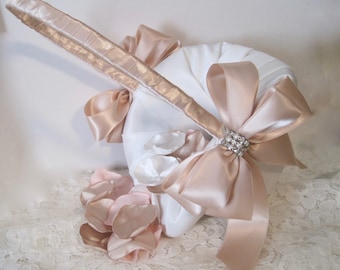 May include: A white satin flower girl basket with a champagne-colored satin ribbon bow and a rhinestone embellishment. The basket is filled with champagne-colored silk flower petals.