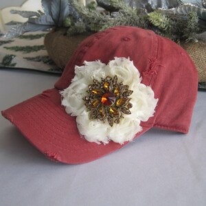 May include: A red baseball cap with a white fabric flower and a gold and orange jeweled brooch.