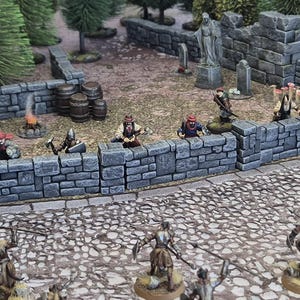 Könnte beinhalten: Miniatur-Fantasy-Diorama mit Steinmauer, Fässern und Kriegerfiguren. Die Szene umfasst ein kleines Lagerfeuer, Bäume und eine Statue und schafft eine detaillierte Tabletop-Spielumgebung. Die Figuren sind wie im Kampf posiert.