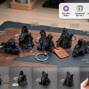 Pode incluir: Um conjunto de cinco porta-chaves em forma de cabeça de dragão preto com acabamento mate e texturas detalhadas. Cada porta-chaves apresenta uma escultura única e inclui ferragens metálicas. Uma etiqueta de couro castanho tem o texto DRACOMIS.
