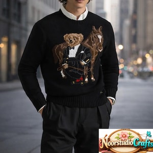 Puede incluir: Suéter negro con un oso con esmoquin y un caballo marrón. El oso sostiene las riendas. El suéter tiene dobladillo y puños acanalados. La persona lleva debajo una camisa blanca con cuello.