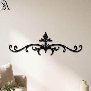Pode incluir: Decoração de parede em metal preto com um design simétrico, apresentando um elemento floral central e detalhes curvos e rodopiantes. A peça decorativa é montada numa parede branca.