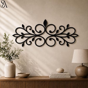 May include: A black metal wall art piece featuring a symmetrical horizontal design with intricate scrollwork, swirling vine patterns, and small leaf-shaped accents. The decorative metal structure is mounted centrally on a plain wall surface.