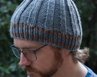 May include: A ribbed knit beanie in shades of gray and brown. The hat features a ribbed design with a contrasting brown band at the brim. The hat is made of a soft, warm material, perfect for cold weather.