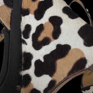 May include: Close-up of a pair of high-heeled shoes with a black leather base and a spotted pattern in white, brown, and black. The shoes have a thin ankle strap and a high heel.