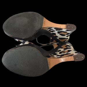 May include: Pair of wedge sandals with a leopard print design. The sandals have a black sole and a strap around the ankle. The wedge heel is approximately 4 1/2 inches high.