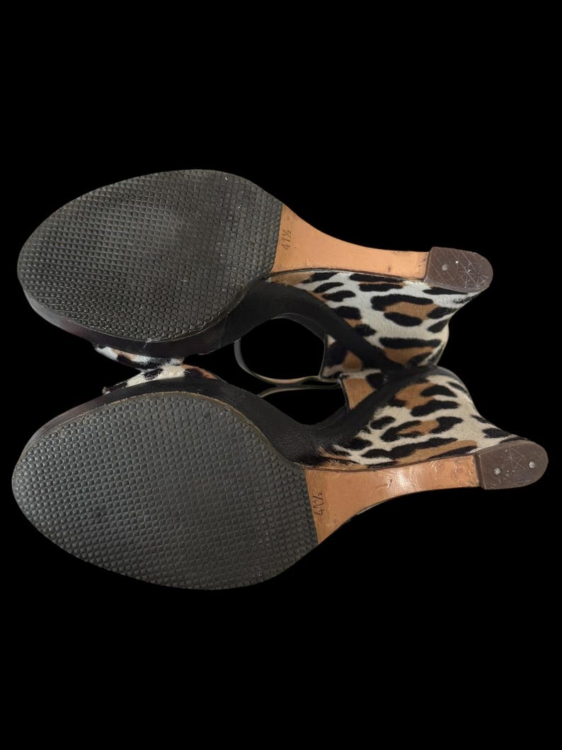 May include: Pair of wedge sandals with a leopard print design. The sandals have a black sole and a strap around the ankle. The wedge heel is approximately 4 1/2 inches high.