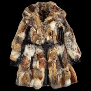 May include: A patchwork fur coat in shades of brown, tan, and cream. The coat has a wide collar and a leather belt at the waist. The sleeves are long, and the coat appears to be knee-length. The fur is a mix of textures.