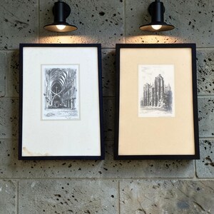 May include: Two rectangular black frames containing black and white architectural sketches of gothic cathedrals. The left frame features a white mount with a cathedral interior, while the right frame has a cream mount with a cathedral exterior view.