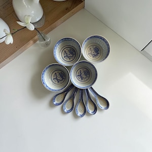 Könnte beinhalten: Ein Set aus vier Keramikschalen und fünf passenden Löffeln, jeweils mit einer cremefarbenen Basis und komplizierten blauen Blumen- und geometrischen Mustern. Die Schalen haben eine abgerundete Form und die Löffel einen geschwungenen Griff.