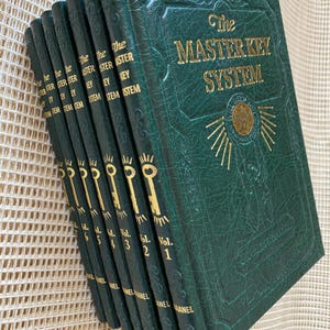 Peut inclure: Une collection de livres à couverture rigide verts intitulés "The Master Key System". Les livres ont des lettres dorées et un motif de clé sur le dos. La couverture présente un motif de soleil doré.