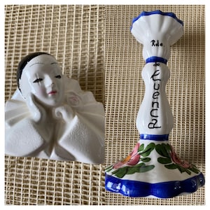 May include: Two ceramic decorative items. One is a white bust of a person with black hair and a white collar. The other is a white candlestick with blue accents, floral designs, and the text "de Cuenca".