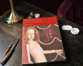 May include: A softcover book titled Yoshida Style Ball Jointed Doll Making Guide by Ryo Yoshida. The cover features a photograph of a pale, realistic doll with long reddish-brown hair against a dark red background with gold line accents.