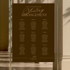 May include: A dark brown rectangular seating arrangement sign with gold text hanging from a gold metal frame. The sign features the header A SEAT SAVED JUST FOR YOU, the title Seating ARRANGEMENT, nine tables with guest names, and the names Maya & Charles.