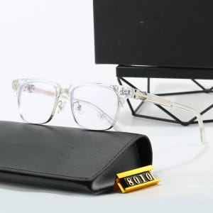 Puede incluir: Gafas con montura transparente y lentes cuadradas, sobre un estuche de cuero negro. Las gafas tienen detalles plateados y un elemento decorativo en las patillas. Una etiqueta dorada con el número "8010" es visible.