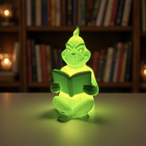May include: A glowing lime green lamp shaped like a seated creature with a pointed head and furrowed brow, holding an open book. The figure has textured fur details, pointed ears, and a mischievous facial expression, emitting a bright light.