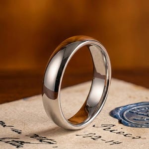 Könnte beinhalten: Ein polierter silberfarbener Ring mit einer glatten, abgerundeten Außenfläche und einer hellbraunen Holzmaserung an der Innenseite, der ein sauberes, reflektierendes Metallfinish und eine natürliche Holzstruktur aufweist.