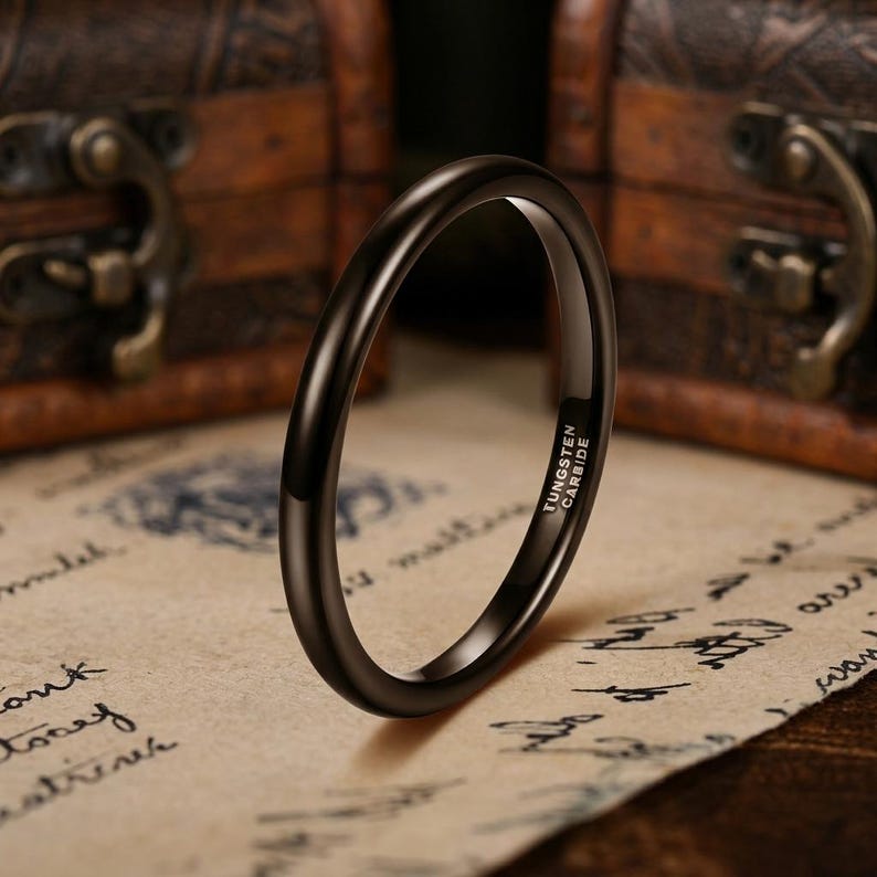Puede incluir: Un anillo negro fino y pulido hecho de carburo de tungsteno. La banda presenta un perfil liso y redondeado con un acabado de alto brillo. El interior del anillo est&aacute; claramente grabado con el texto TUNGSTEN CARBIDE en una fuente sans-serif.