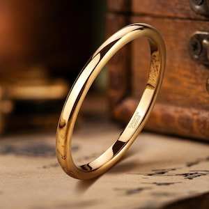 Puede incluir: Un anillo de tono dorado pulido con una banda lisa y redondeada. El interior de la banda presenta el texto grabado Tungsten Carbide, que indica la composici&oacute;n del material de esta pieza de joyer&iacute;a circular simple para el dedo.