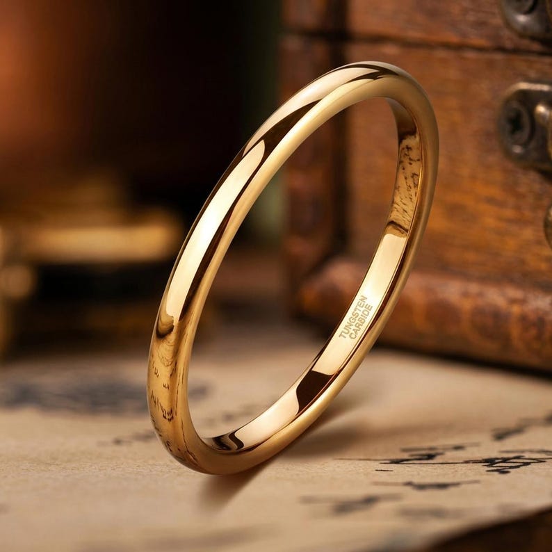 Puede incluir: Un anillo de tono dorado pulido con una banda lisa y redondeada. El interior de la banda presenta el texto grabado Tungsten Carbide, que indica la composici&oacute;n del material de esta pieza de joyer&iacute;a circular simple para el dedo.